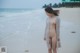 A naked woman standing on a beach next to the ocean.