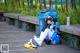 A woman sitting on a wooden bench next to a trash can.