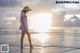 A woman in a white dress and hat walking on the beach.