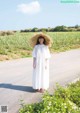 A woman in a white dress and straw hat standing on a road.