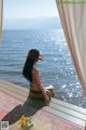 A woman sitting on a wooden deck looking out over the water.