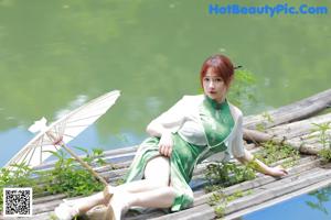 A woman in a green dress sitting on a wooden dock.