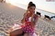 A woman in a pink dress sitting on a beach.