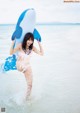 A woman in a bikini holding an inflatable shark in the ocean.