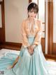 A woman in a blue and orange dress sitting on a bed.