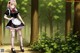 A woman in a maid outfit standing in the woods.